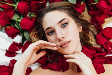 overhead view of attractive woman looking at the camera lying on the bed with roses in the hair.の写真素材