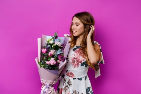 young woman holding bouquet of eustoma flowers and touching hair on purple background.の写真素材