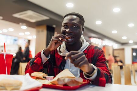 African man is eating chicken nuggets in a restaurant and enjoying delicious foodの写真素材