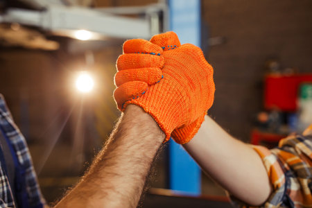 close up of mechanics shaking hands in the gloves in the garage, sun effect.