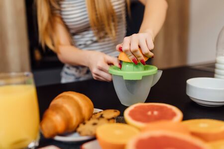Close up photo, beautiful young woman making fresh orange juice in kitchen.の写真素材
