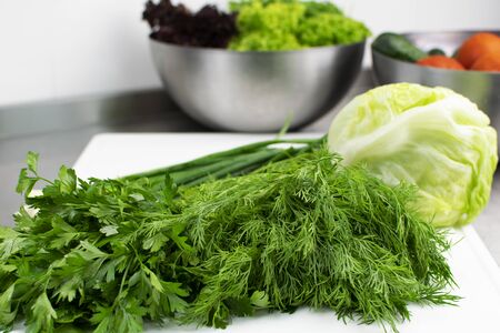 Fresh greens and cabbage close-up on a cutting board, in the background lettuce and vegetables in a metal bowlの写真素材
