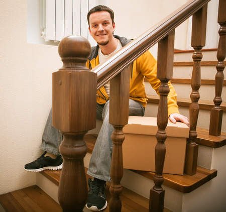 Moving house. Young man with cardboard boxes on a stairs.の写真素材