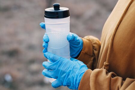 COVID-19 Pandemic Coronavirus girl in blue gloves holding a bottle of water on a jog during coronavirusの写真素材