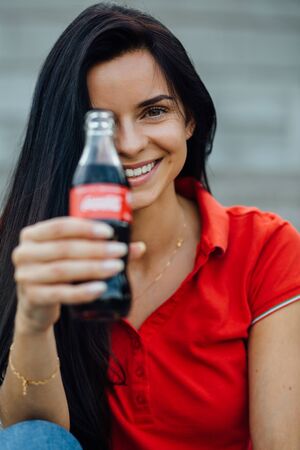 Close up of beautiful young smiling woman in red t-shirt enjoying drinking colaの写真素材