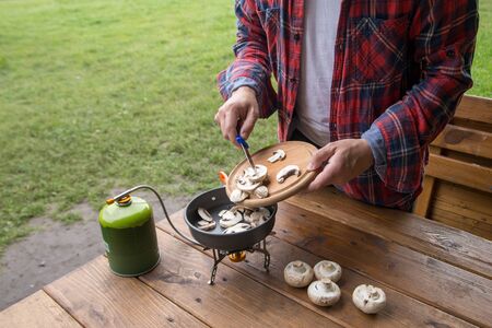 man slices mushrooms champignons for cooking at the campsiteの写真素材