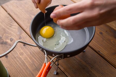 girl breaks an egg to cook omlene on a picnic at the campsiteの写真素材
