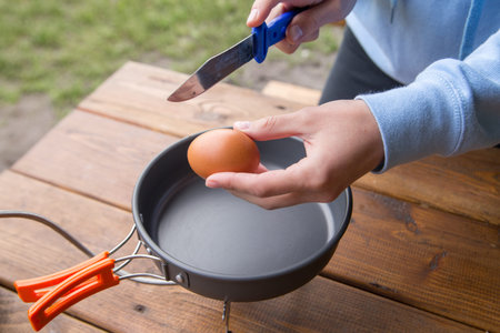 girl breaks an egg to cook omlene on a picnic at the campsiteの写真素材