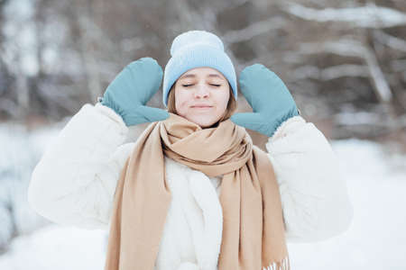 beautiful girl in a white fur coat on a blue hat in a snowy winter forestの写真素材