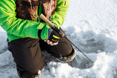 young man on a winter fishing trip on a snowy lake fishes on a fishing rodの写真素材