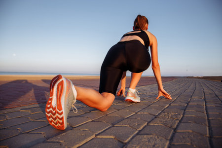 girl runner in a black tracksuit and sneakers runs by the sea during sunset