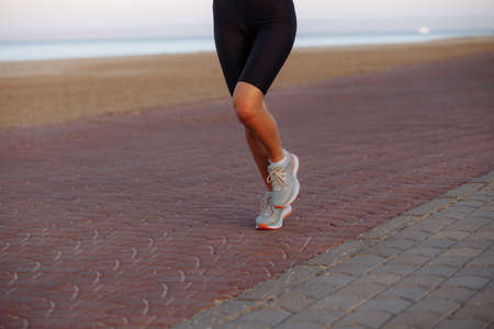 girl runner in a black tracksuit and sneakers runs by the sea during sunsetの写真素材