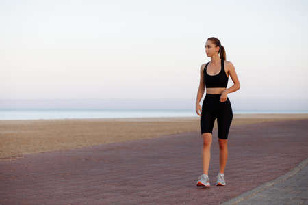 girl runner in a black tracksuit and sneakers runs by the sea during sunsetの写真素材