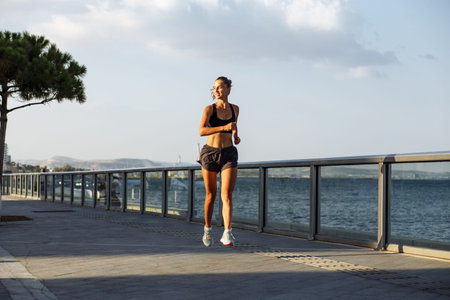 beautiful fitness girl in shorts and sports top runs on the waterfront by the sea during sunset