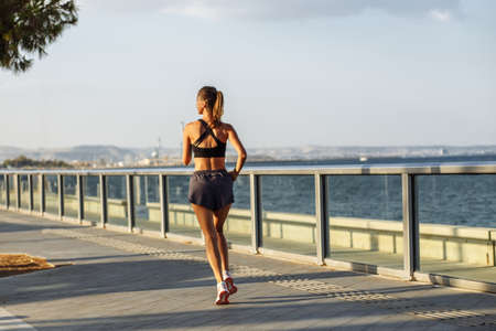 beautiful fitness girl in shorts and sports top runs on the waterfront by the sea during sunsetの写真素材