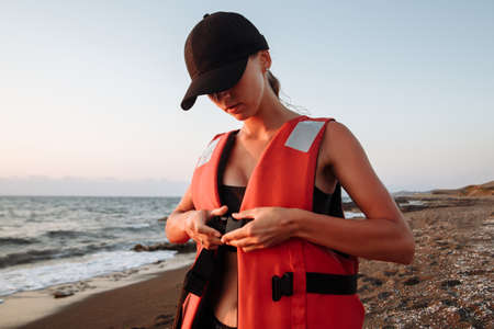 beautiful girl in a black swimsuit wears a life jacket on the beachの写真素材