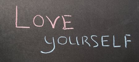 Inscription love yourself on a dark board with pink and blue chalkの写真素材