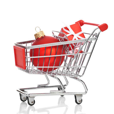 Shopping trolley with gift box and red christmas ball isolated on white background, with reflection.の写真素材