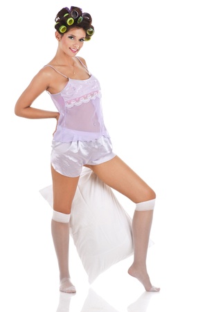 Portrait of a lovely young woman with hair rollers holding a pillow isolated on white backgroundの写真素材