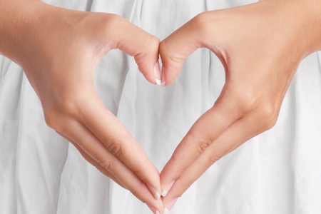 The form of heart shaped by female hands on a white dress backgroundの写真素材