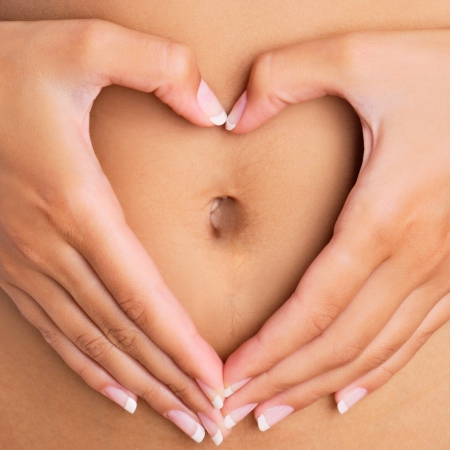 A woman's hands forming a heart symbol around navel の写真素材