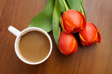 White cup of coffee with red tulips on wooden table の写真素材