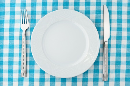 Empty dinner plate with fork and knife on blue and white checked gingham tablecloth の写真素材