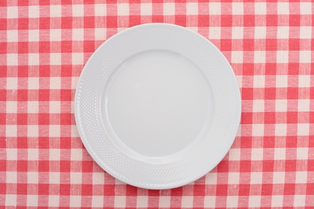 Empty dinner plate on red and white checked gingham tablecloth 
の写真素材