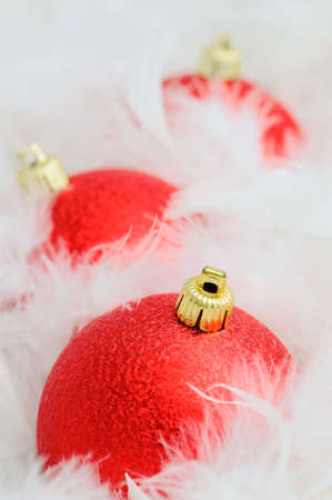 Three bright red christmas bulbs on white fluffy feathersの写真素材