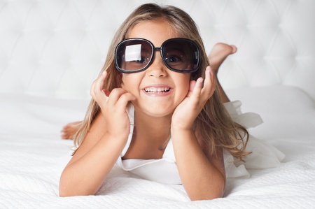 Portrait of cute girl with eyewear lying barefoot in the bedの写真素材