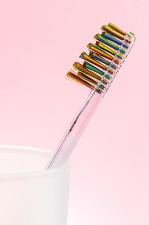 Toothbrush with varicolored brisle in white cup over pink background の写真素材