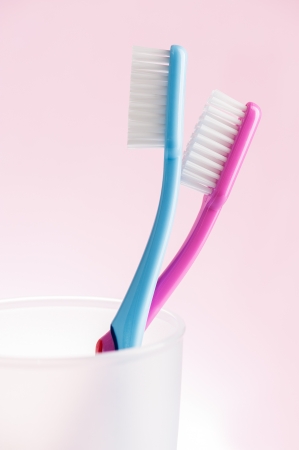 Pink and blue toothbrushes in white plastic glass over pink background の写真素材
