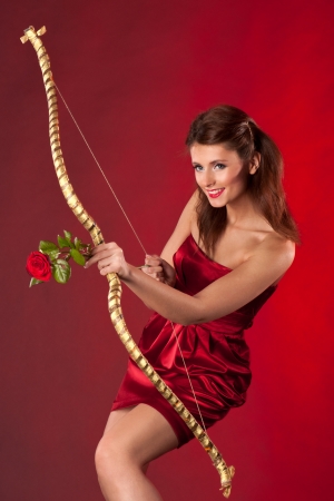 Young woman with bow and red rose as arrow on red background   Concept for Valentineの写真素材