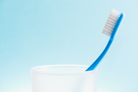 Blue toothbrush in white plastic glass over blue background.の写真素材