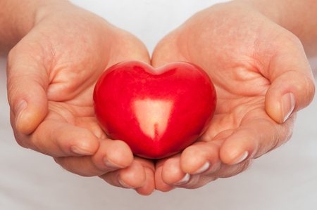 Man with red heart in his hands over body background の写真素材