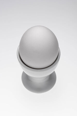 Single white egg in a ceramic eggcup on a white background.の写真素材