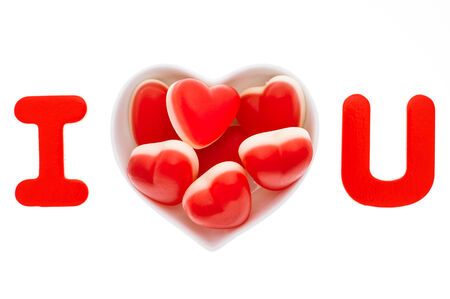 Red heart shaped sweets in the white heart shaped plate isolated over white. 'I love you' concept.の写真素材