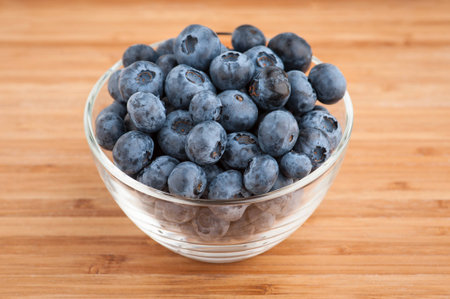Blueberries in a glass bowl on wooden table, close-up. の写真素材