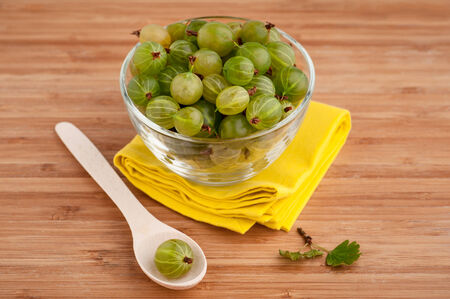 Gooseberries in a glass bowl with wooden spoon and yellow napkin on table, close-up. の写真素材