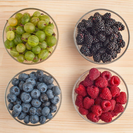 Variation of berries (gooseberry, blackberries, blueberries, raspberries) in a glass bowls on wooden table, close-up. の写真素材