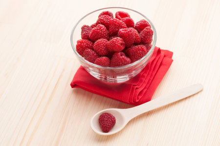 Raspberries in a glass bowl with wooden spoon and red napkin on the table, close-up. の写真素材