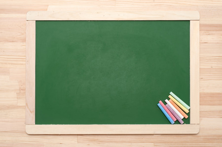Closeup of blank green blackboard with pieces of coloured chalks on wooden surface.の写真素材