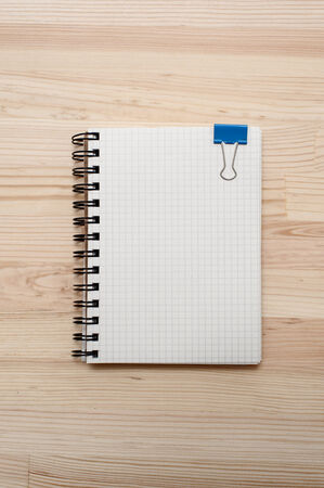 Checked notebook with blue binder clip on wooden background.の写真素材