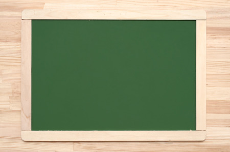 Green blackboard with frame on wooden surface.の写真素材
