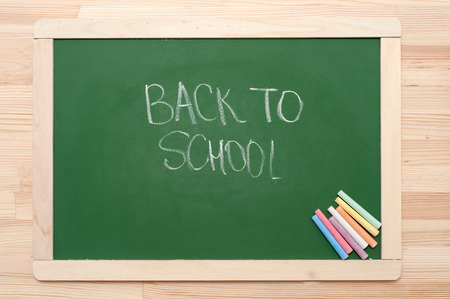 Closeup of blank green blackboard with pieces of coloured chalks and "back to school' text, on wooden surface.の写真素材