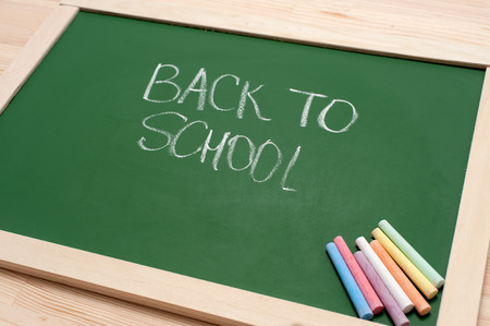 Closeup of blank green blackboard with pieces of coloured chalks and 'back to school' text on wooden surface. Angle view.の写真素材