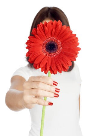 Hiding behind the gerber. Young woman holding a red gerber in front of her face while standing against pure white background.の写真素材
