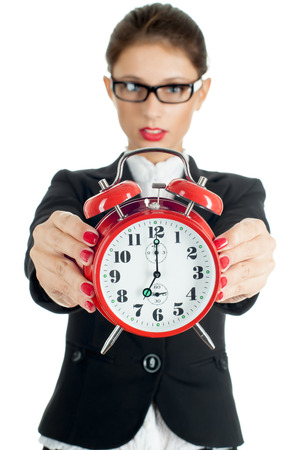 Woman holding out a clock showing 7 o'clock isolated on white. Focus is on alarm.の写真素材