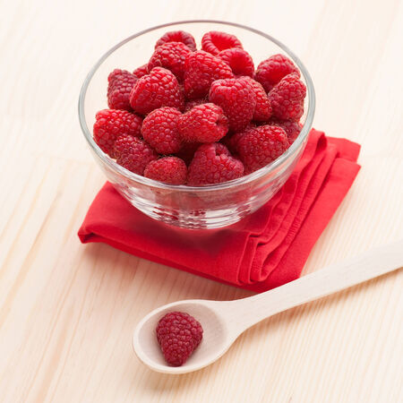 Raspberries in a glass bowl with wooden spoon and red napkin on the table, close-up.の写真素材