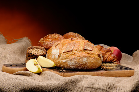 Assortment of baked bread with wheet and apples arranged on coarse textured woven fabric.の写真素材